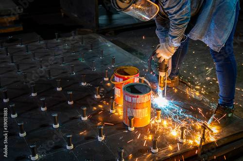 A welder is using a Stud Welding Machine to weld stud bolt on steel plate, at industrial factory.