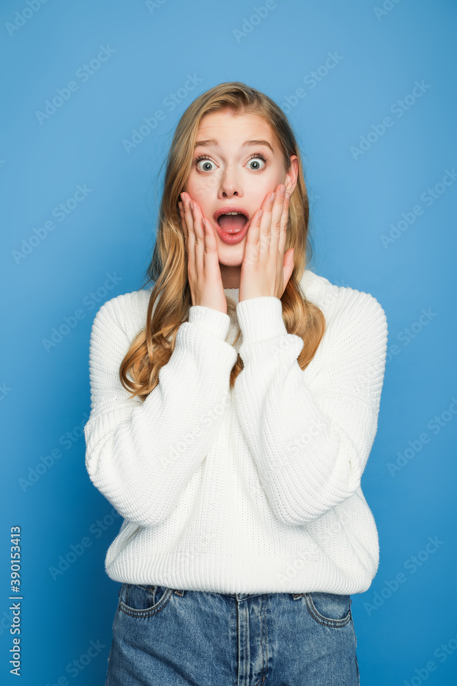 scared blonde beautiful woman in sweater isolated on blue background scared blonde beautiful woman in sweater isolated on blue background