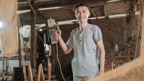 carpenter stands holding a wooden stake smiling when he sees the camera at the workshop