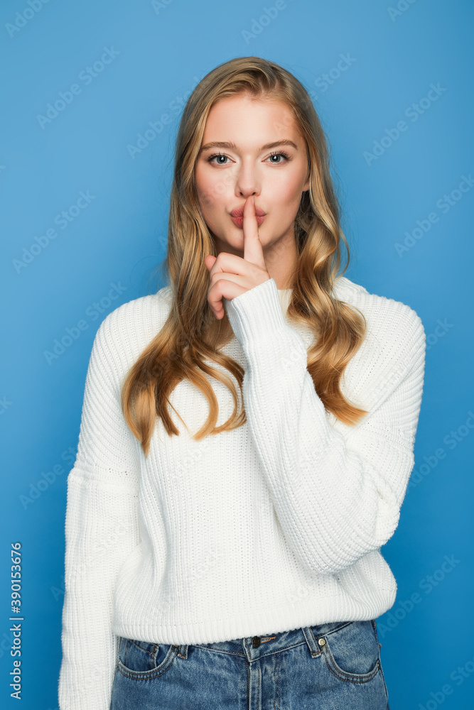 blonde beautiful woman in sweater showing shh isolated on blue background blonde beautiful woman in sweater showing shh isolated on blue background