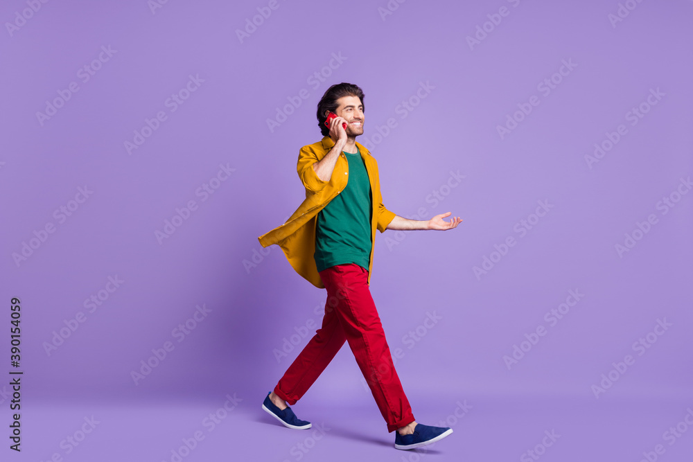 Full length photo portrait of man talking over phone walking isolated on vivid violet colored background
