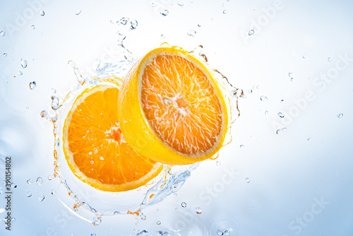 Two halves of orange fruit splashing into clear water.