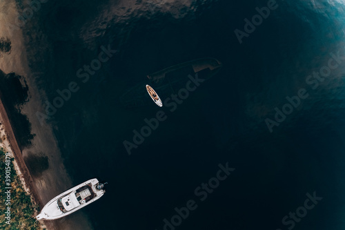 Aerial view from a drone to a boat on the lake and a girl on a stand-up paddle over a sunken ship in Altai
