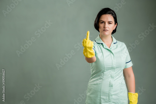 Young cleaning woman wearing a green shirt and yellow gloves showing fuck you © Cipri Suciu 