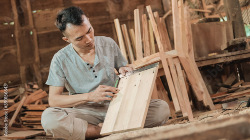 carpenter sitting on the floor holding a carpenter elbow ruler while measuring wood in a workshop