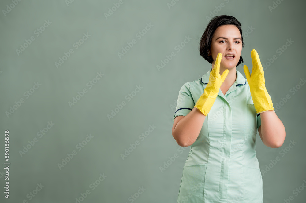 Young cleaning woman wearing a green shirt and yellow gloves shouting with her hands to her mouth Young cleaning woman wearing a green shirt and yellow gloves shouting with her hands to her mouth