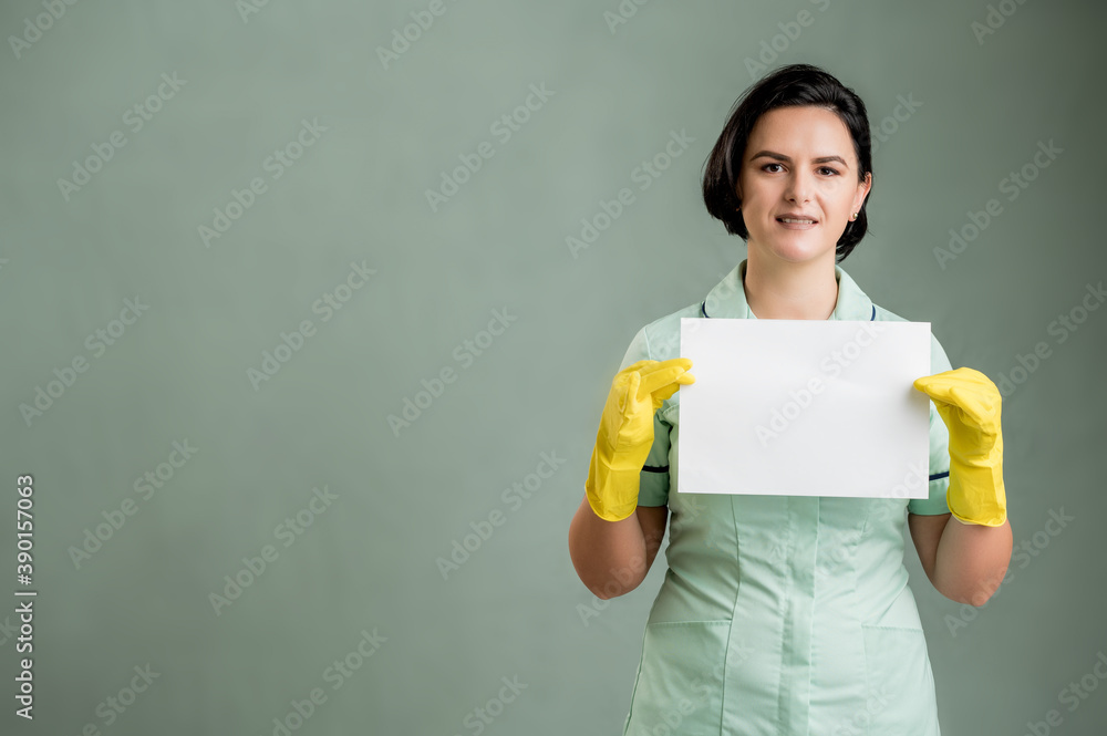 Young cleaning woman wearing a green shirt and yellow gloves holding a white paper Young cleaning woman wearing a green shirt and yellow gloves holding a white paper
