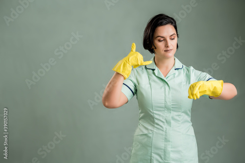 Young cleaning woman wearing a green shirt and yellow gloves showing it's time gesture © Cipri Suciu 