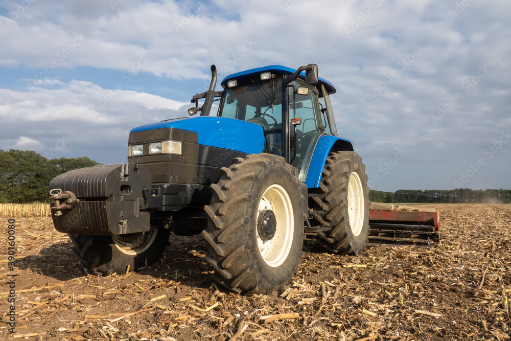 Big blue modern tractor in the field. Cultivating land after harvest Big blue modern tractor in the field. Cultivating land after harvest