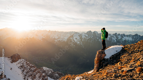 Climber looking at a snowy mountain landscape in a sunny winter day. Travel man tourist alone on the edge cliff mountains and looking on the valley. Adventure lifestyle extreme vacations.