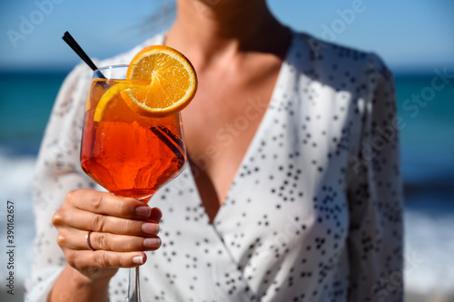 Woman in white dress holding a red cocktail with orange slice at the sea