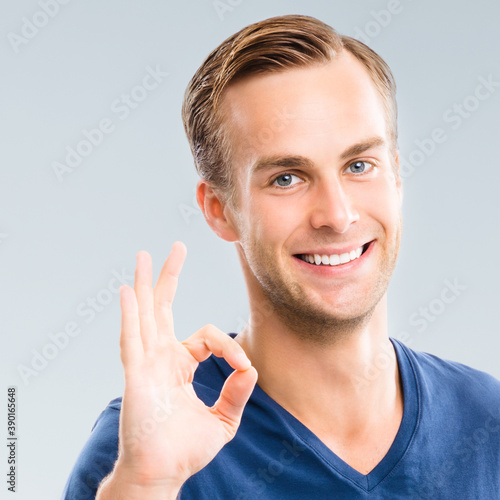 Portrait of cheerful young man showing okay ok gesture, isolated over grey background. Emotions and success studio concept. Square composition. photo