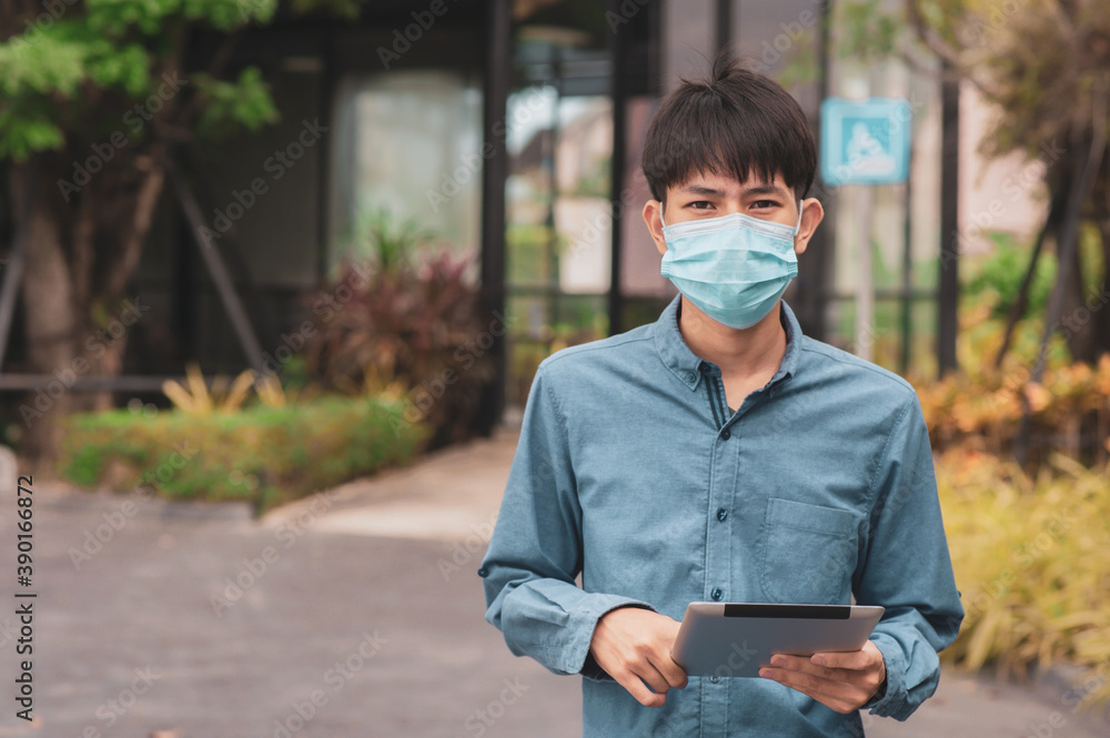Asian man wearing face mask protect coronavirus COVID 19 and Holding tablet