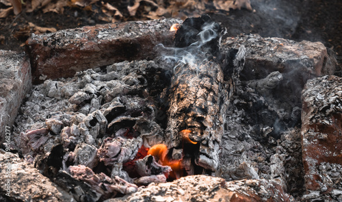 A small flame is barely visible in the dying fire. Light a fire in the woods. Smoldering wood in the fire, hot coals and a lot of smoke.