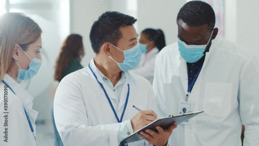 Diverse multi-race adult team of doctors discussing medical report writing notes sharing ideas treatment medation talking in the hospital corridor. Healthcare facilities. Clinic. Cooperation Diverse multi-race adult team of doctors discussing medical report writing notes sharing ideas treatment medation talking in the hospital corridor. Healthcare facilities. Clinic. Cooperation