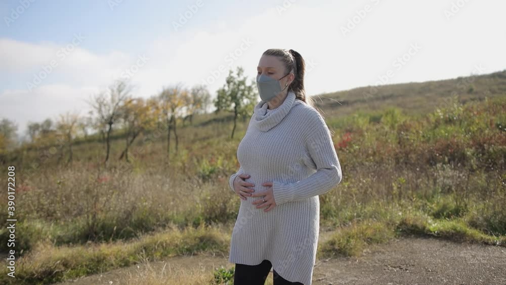 Young pregnant woman walking in the nature and wearing safety face mask in pandemics Young pregnant woman walking in the nature and wearing safety face mask in pandemics