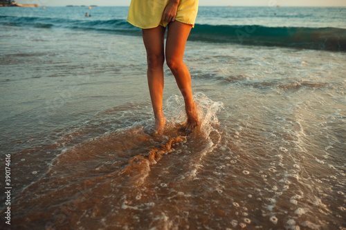 A young girl walks on the seashore in the rays of the setting sun A girl is dressed in a yellow sundress © toxicoz