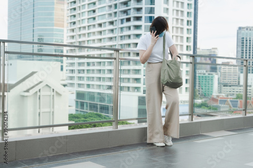 solo asian woman wear protective mask during use phone and relax at rooftop with city background