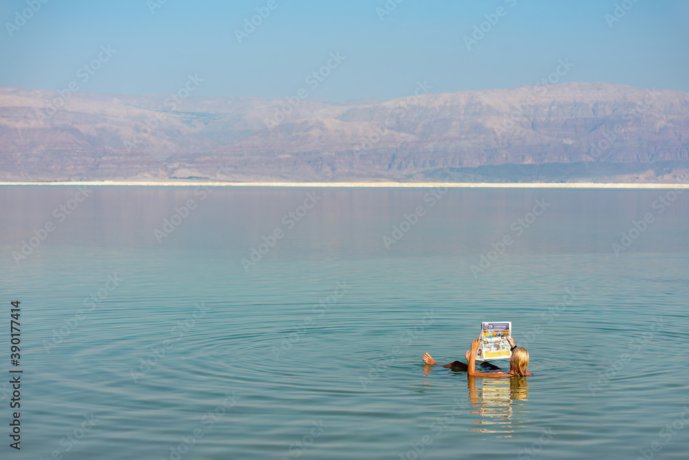 A woman floating in the water of the dead sea while reading a newspaper.