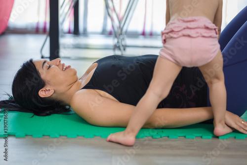 mother lying down doing yoga while little girl plays with her