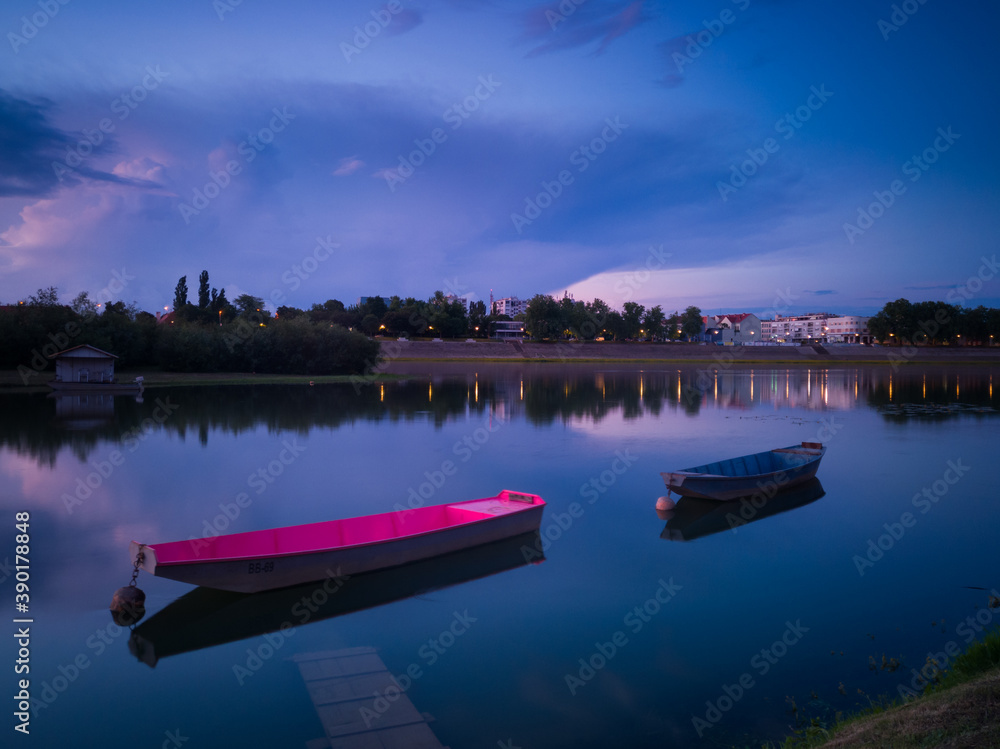 The landscape of the Sava River in summer, moored boats along the shore and a large ominous cumulonimbus cloud above the horizon at dusk