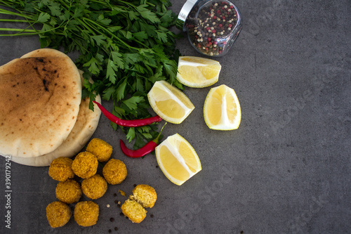 Fresh made falafels on dark grey table with lemon slices, chili pepper and parsley. Authentic food of Israel. Ingredients top view photo. Healthy eating concept. 