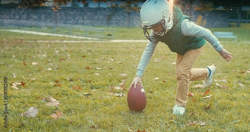 Cheerful happy child in helmet playing American football outdoors in sunny day at public park. Family sports weekend. 4K video.
