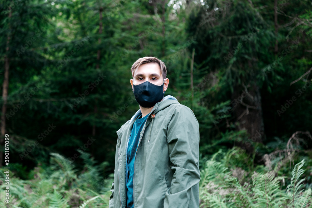 Man in mask travel alone keeping social distance in local tourism. Protection against coronavirus, covid 19. Man in black protective medical mask outside in forest alone. Man in mask travel alone keeping social distance in local tourism. Protection against coronavirus, covid 19. Man in black protective medical mask outside in forest alone.