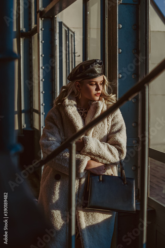 Outdoor fashion portrait of elegant woman wearing faux fur teddy bear coat, leather beret, holding black classic handbag, posing in street of city. Autumn, winter trendy outfit