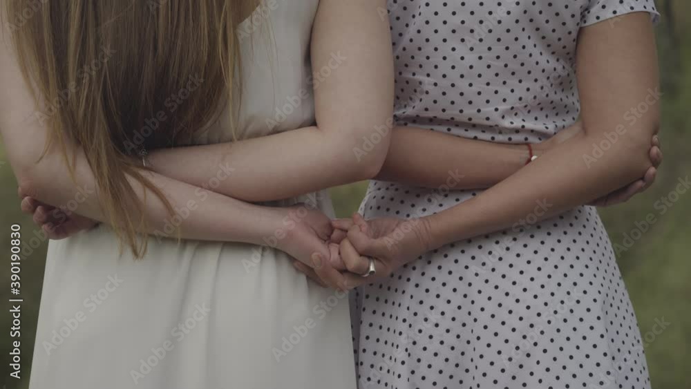 Back view of unrecognizable adult women taking each other's palms. Slim young Caucasian ladies holding hands on windy day outdoors. Unity and support concept. Back view of unrecognizable adult women taking each other's palms. Slim young Caucasian ladies holding hands on windy day outdoors. Unity and support concept.
