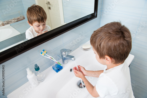 one person little caucasian healthy cute kid in white shirt washing his hands under fresh water in washbasin in blue bathroom at home