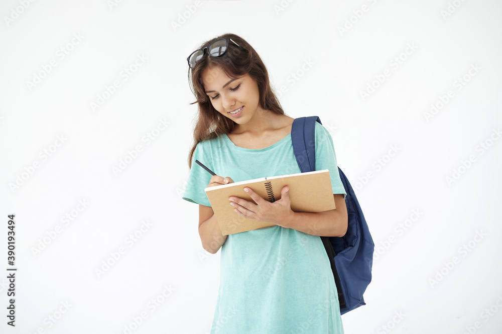 People, education and future concept. Isolated portrait of charming mixed race female student carrying bag on one shoulder and making notes in copybook during lecture on economics at college People, education and future concept. Isolated portrait of charming mixed race female student carrying bag on one shoulder and making notes in copybook during lecture on economics at college