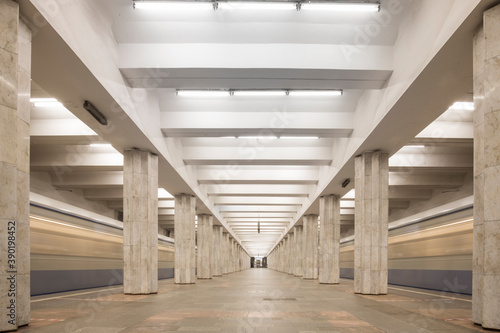 Linear perspective view of an underground station with two rows of multiple columns and blurred traces of trains going in both directions. No people