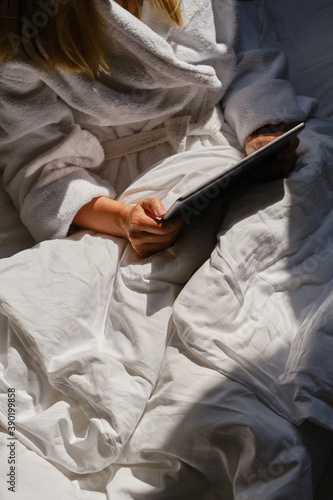 Woman holds tablet in hands. Relaxed in bed. Morning online activities in home. Watching movies and TV shows on mobile device. Social media addiction. Work at home, freelance. Technology in lifestyle
