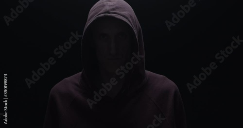 Silhouette of a man with a darkened face in a hood on a black background. A portrait of a murderer, a hacker.