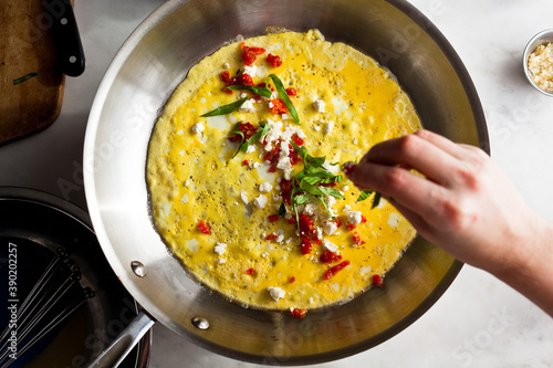 Overhead view of woman spreading basil leaves on egg omelet cooking in pan photo