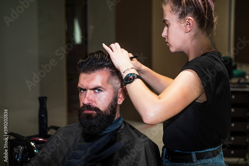 attractive barber making haircut of handsome male in barbershop, hairdressing tools