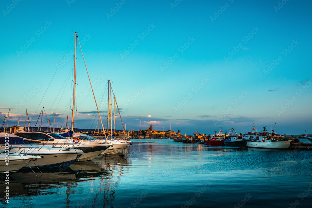Boats in Alghero harbor under a clear sky at sunset