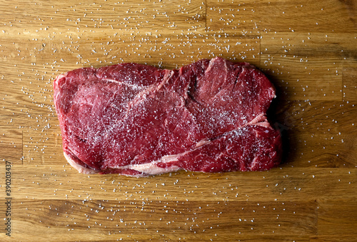 Close up of raw meat steak seasoned with kosher salt on wooden table