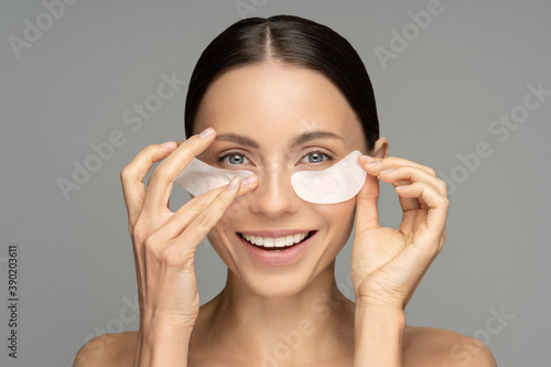 Fototapete Happy woman applying hydrogel under-eye recovery patches enriched with collagen, vitamin E, provides intensive hydration and diminishes the signs of aging, helps reduse eye puffiness