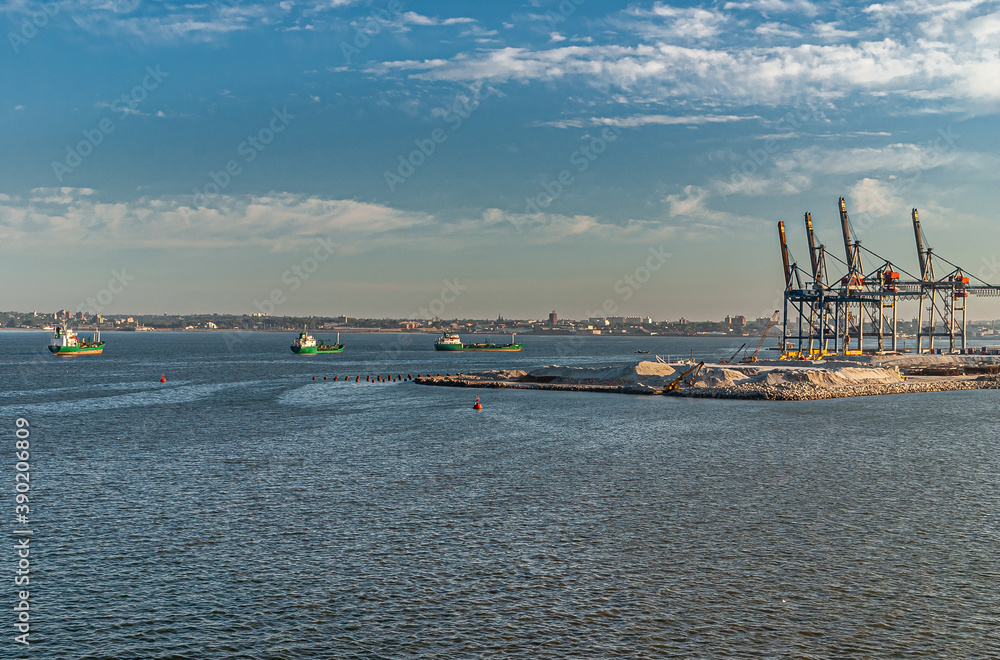 Montevideo, Uruguay- December 18, 2008: Ships and ranes at shipping container terminal in port with expansion works in blue Rio de la Plata water and under ligh blue morning sky.