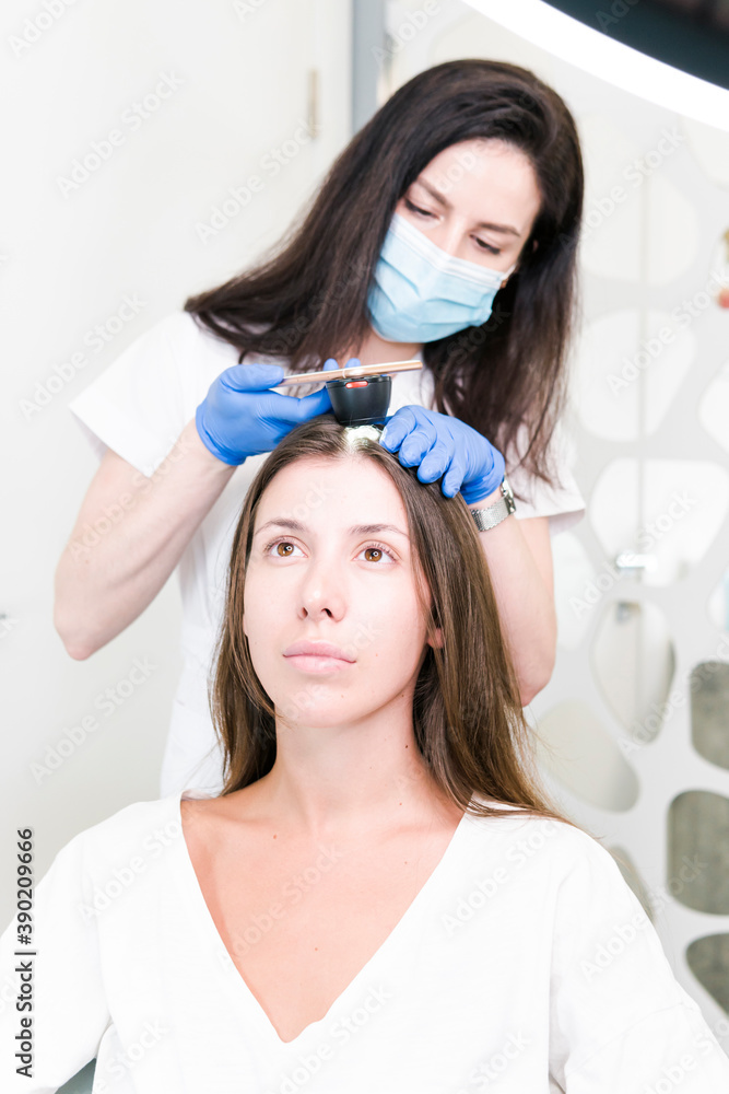 The doctor dermatologist examining client hair with a special apparatus for diagnostic hair. Trichoscopy procedure in the trichology clinic. Concept of health care. The doctor dermatologist examining client hair with a special apparatus for diagnostic hair. Trichoscopy procedure in the trichology clinic. Concept of health care.