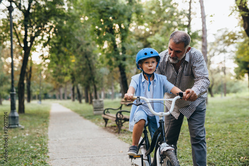 Foto boy teaching to ride bike with his grandfather in public park