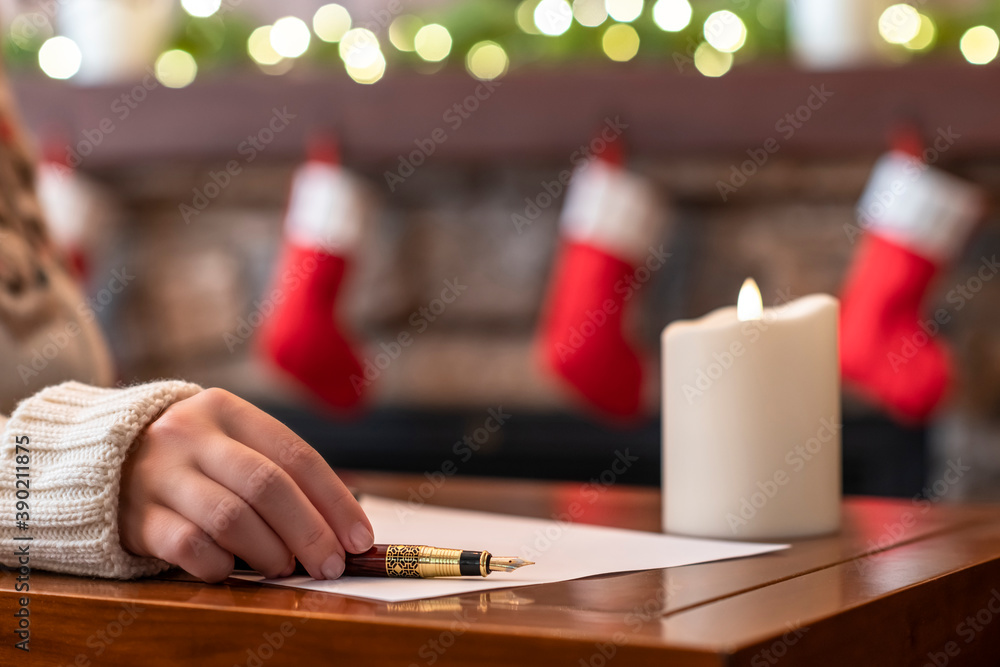 Woman writing wish list using fountain pen on sheet of paper at christmas fireplace with decoration of light bulbs and candle on table. Woman writing wish list using fountain pen on sheet of paper at christmas fireplace with decoration of light bulbs and candle on table.