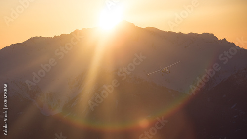A single engine airplane flying through snowy mountains at sunset