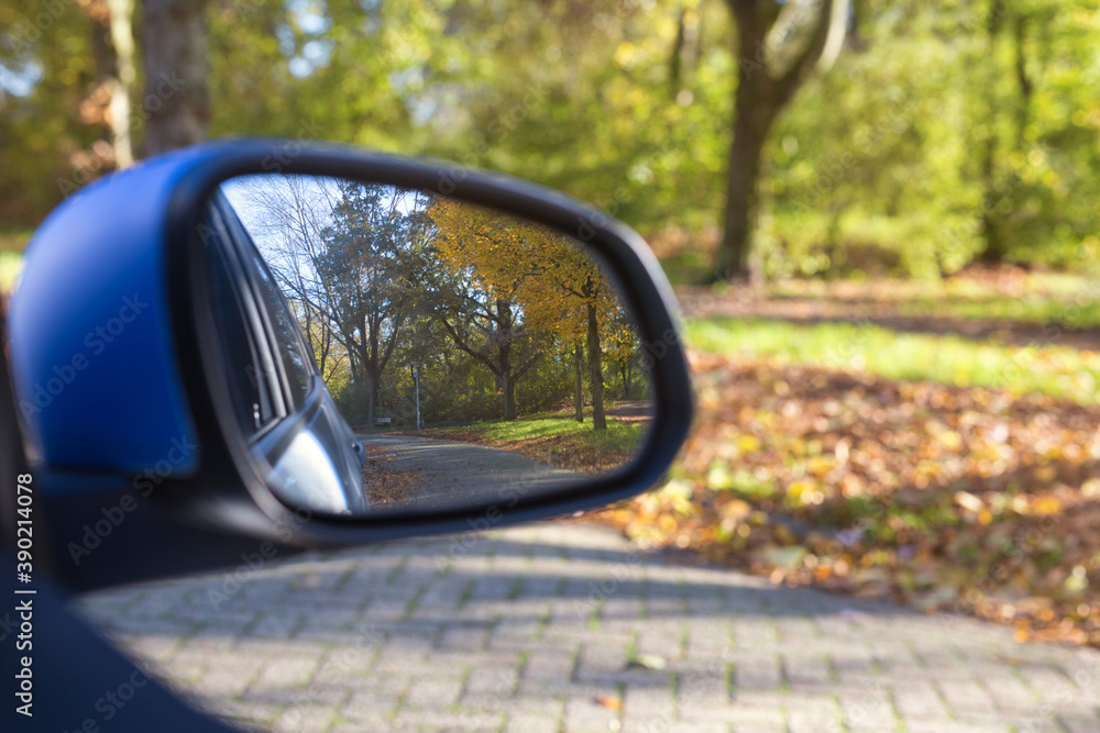 Car mirror Closeup with beautiful autumn landscape in reflection, on the road with the car on empty road blurred background