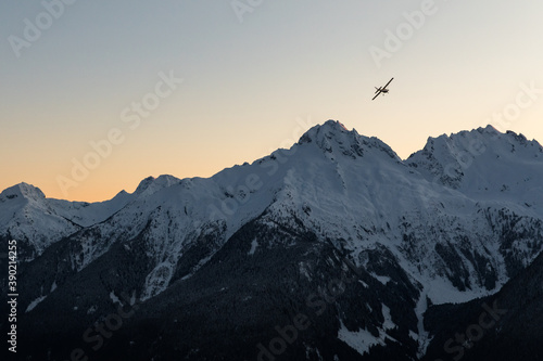 A single engine airplane flying through snowy mountains at sunset