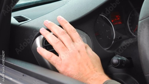 The driver's hand controls the direction of movement of ventilation and air conditioning air on a black shiny car dashboard.