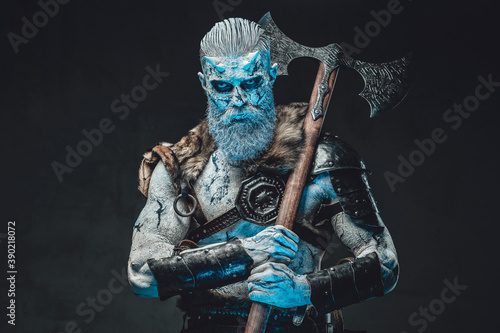 Northern risen from the dead chief in dark armour with fur with iced skin and blue eyes holding axe on his shoulder in moonlight.