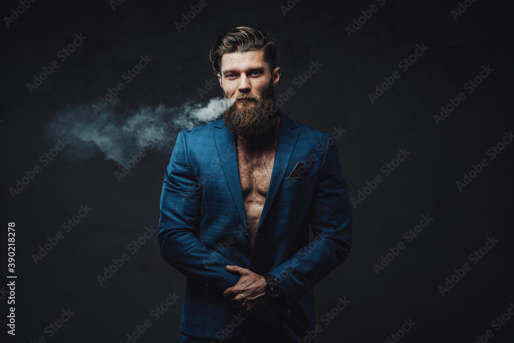 Styled and cool gentleman with beard and stylish haircut posing smoking vape in dark background.